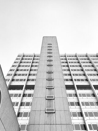 The same tower in black and white, grey concrete and rows of windows against a white sky.