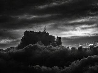 The same cloud in black and white, nearly black against a sky of dark streaked cloud with light breaking through at the right.